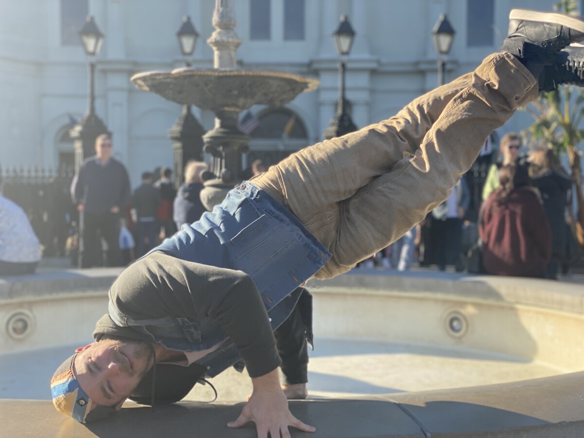 Breakdancer balancing on one hand in front of the fountain in Jackson Square with St. Louis Cathedral behind him, New Orleans