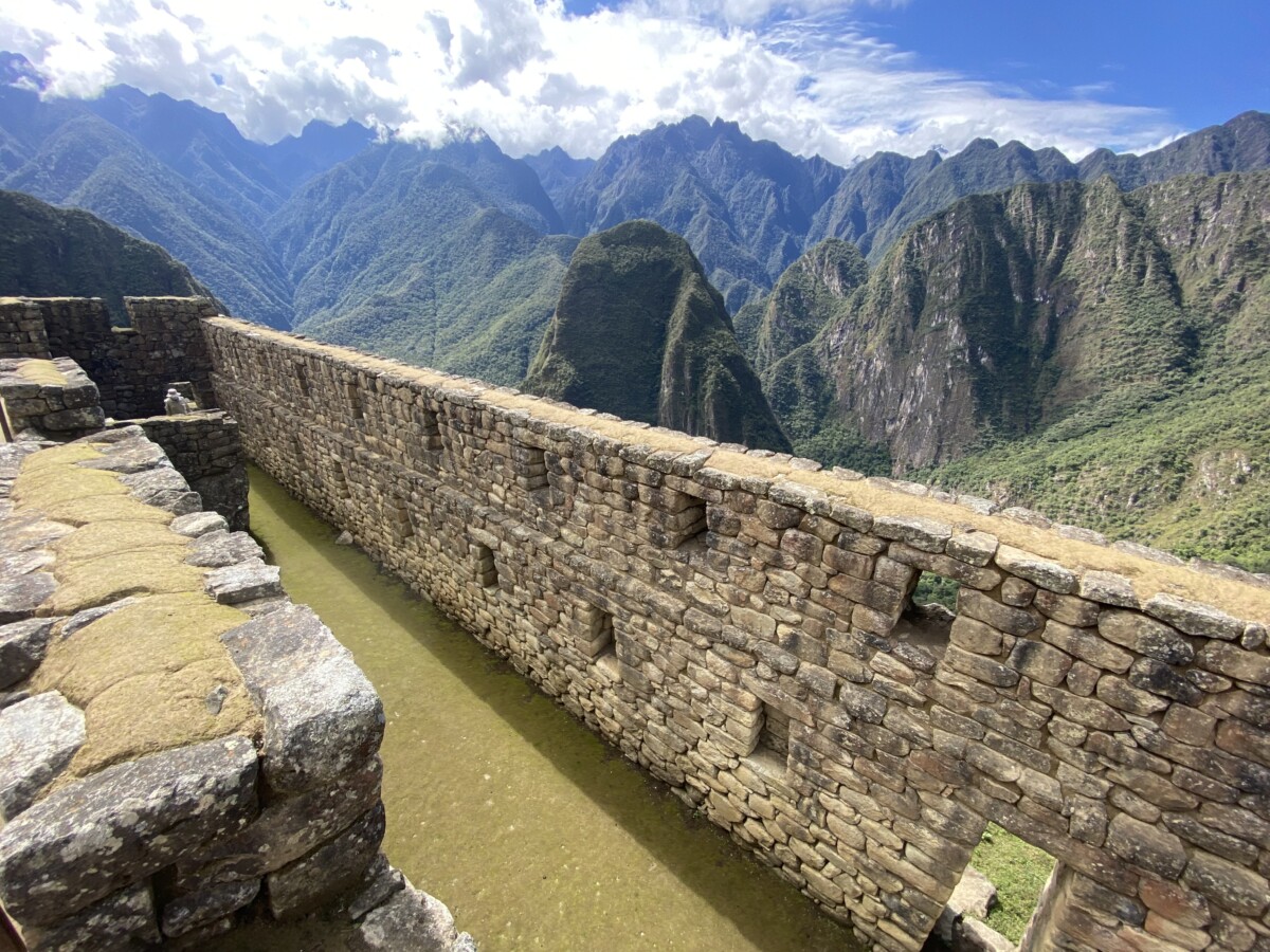 A long Inca stone wall with a water channel running alongside it, overlooking the Urubamba valley at Machu Picchu